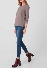 Top de manga tres cuartos con estampado de pata de gallo en burdeos y blanco, combinado con jeans ajustados azules y botines burdeos de tacón cuadrado.