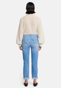 Maglione lavorato a maglia di un beige chiaro con maniche a palloncino abbinato a jeans in denim blu chiaro. I jeans mostrano una leggera scoloritura e sono risvoltati a livello delle caviglie.