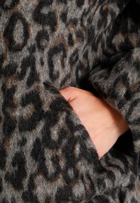 Cappotto a stampa leopardata in morbido e strutturato misto lana grigio e nero con accenti marroni; mano poggiata nella tasca laterale nascosta.