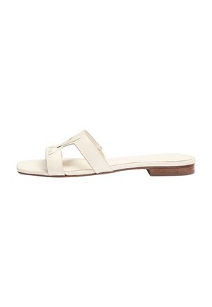 Sandalia plana beige con una tira ancha con diseño de recortes y un tacón bajo de madera marrón sobre un fondo blanco.