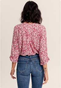 Rote und weiße gemusterte Bluse mit Dreiviertelärmeln, lockerer Passform und Raffung hinten, kombiniert mit blauen Jeans mit mittlerer Bundhöhe.