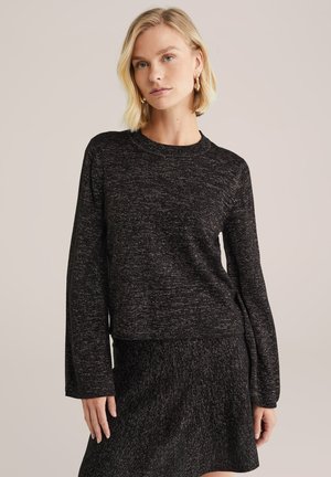 Schwarzer Strickpullover mit langen Ärmeln, rundem Ausschnitt, strukturiertem Stoff und subtilen Sprenkeln, kombiniert mit einem passenden strukturierten Rock.