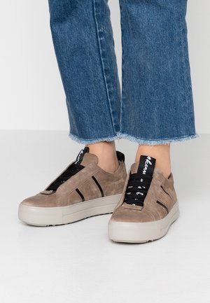 Harmaat nubukista valmistetut slip-on-tennarit, joissa on mustat nauhat, kaksi mustaa raitaa ja teksturoitu kumipohja. Yhdistettynä lyhyisiin sinisiin farkkuihin.