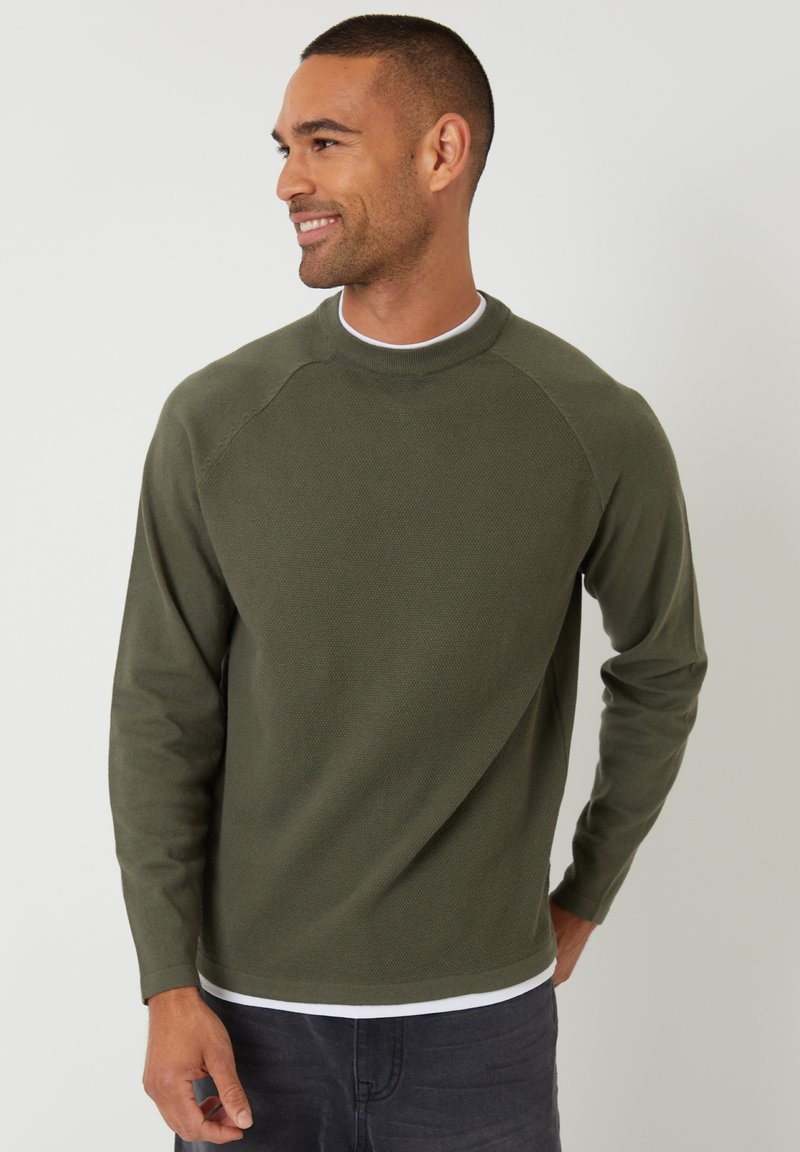 Groene sweatshirt met lange mouwen en een gestructureerde afwerking, ronde hals en raglanmouwen, gelaagd over een wit shirt.