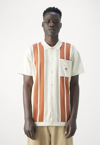 Polo de manga corta con rayas verticales en crema y óxido, con un bolsillo en el pecho y cierre de botones. Elaborado en un tejido de punto texturizado.