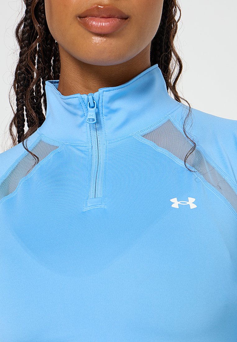 Maglietta sportiva azzurro chiaro con collo zip, caratterizzata da dettagli in rete sulle spalle e un piccolo logo bianco sul petto.