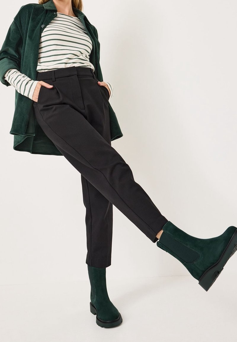 Chemise en velours côtelé verte, haut à manches longues rayé, pantalon noir cintré et bottines vertes à semelle épaisse, présentés sur un fond neutre.