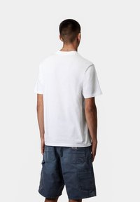 Camiseta de algodón blanca con manga corta, escote redondo, diseño liso. Combinada con pantalones cortos tipo cargo azul con múltiples bolsillos.