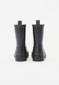 Čierne gumové členkové čižmy s hladkým povrchom, vertikálnymi ryhami a pútkami na obúvanie. Podrážky sú ploché s jemným vzorom.