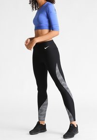 Niebieski, długi rękaw, krótka bluzka oraz czarne legginsy z teksturowanym, białym geometrycznym wzorem. Oba elementy posiadają logo Nike.
