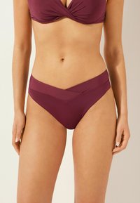 Bas de bikini bourgogne avec un design de taille croisée, fabriqué à partir d'un tissu lisse et extensible. La coupe offre une taille modérée.