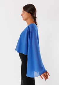 Top blu leggero e trasparente con maniche ampie e una vestibilità fluida, abbinato a pantaloni neri aderenti. Texture morbida, scollatura rotonda.