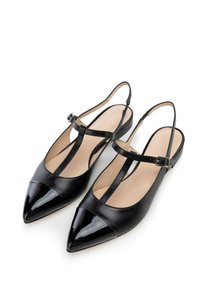 Bailarinas negras con tira detrás y punta afilada, que presentan una brillante puntera, parte superior de cuero suave y correa ajustable con hebilla dorada.