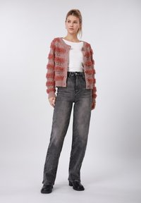 Πλεκτή ζακέτα με ρίγες σε ροζ και κοραλλί απόχρωση, με μακριά μανίκια και κουμπιά· συνδυασμένη με ψηλόμεσα ξεθωριασμένα γκρι τζιν και μαύρες μπότες.