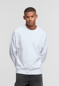 White long-sleeve T-shirt with a relaxed fit and round neckline, made from cotton. Slightly dropped shoulders and smooth texture.