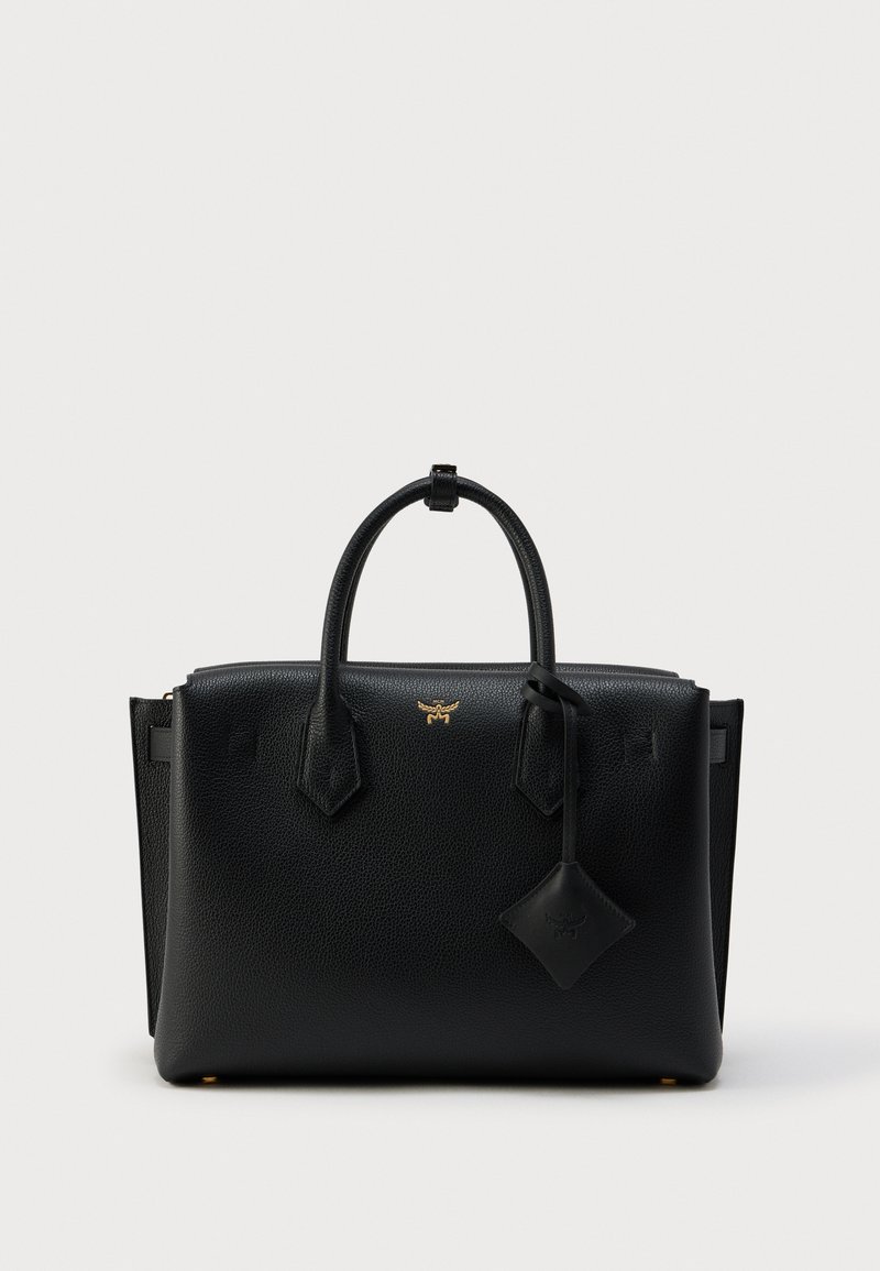 Μαύρη δερμάτινη τσάντα με υφή, διπλές λαβές, χρυσ ή λεπτομέρεια λογότυπου και δερμάτινη ταμπέλα που κρέμεται από μία λαβή, σε απλό φόντο.