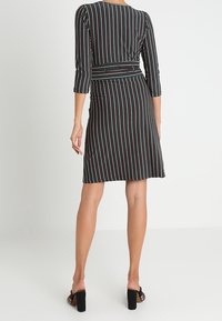 Černé šaty s barevnými vertikálními pruhy, tříčtvrteční rukávy, přiléhavý pas a rozšířená sukně. Hladká tkanina s jemnou texturou.