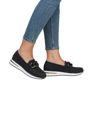 Zapatos negros de slip-on con una parte superior texturizada, que presentan un nudo decorativo y una suela blanca a rayas. Llevados con unos jeans ajustados azules.