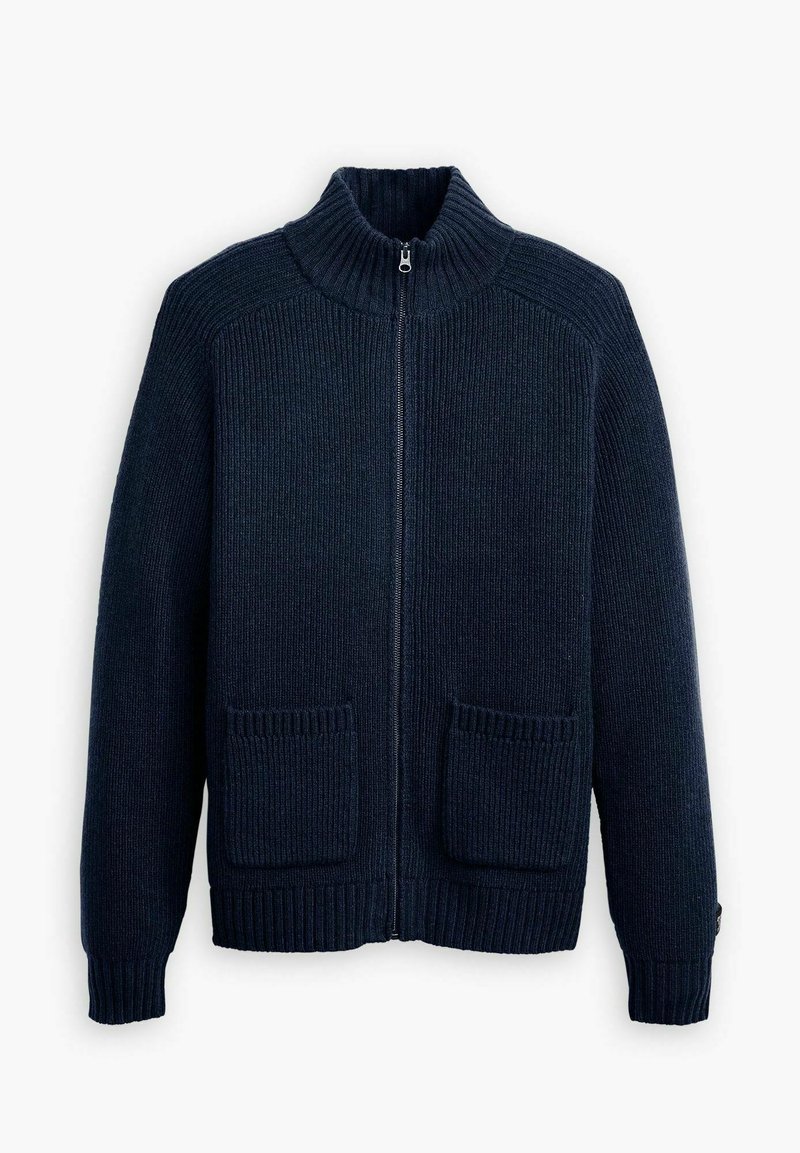 Cárdigan de punto azul marino con cremallera y cuello alto, textura canalé y dos bolsillos parches frontales. Presenta puños y dobladillo de canalé.