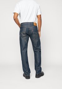 Vaqueros de mezclilla azul oscuro con un corte recto, bolsillos traseros visibles, costura en contraste y una etiqueta de cuero marrón en la cinturilla.