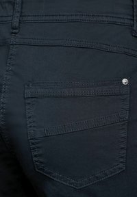 Tmavé džíny z denimu s zadní kapsou, která má jemný vyšitý design a malou kovovou ozdobu. Hladká textura, těsný střih.