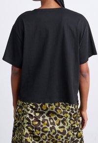 Camiseta negra recortada de manga corta, fabricada en algodón. La parte trasera tiene una textura suave, combinada con una falda de estampado de leopardo en tonos verde y marrón.