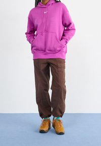 Pink hoodie with kangaroo pockets and drawstrings, paired with brown cargo pants. Shoes are orange with teal accents and black soles.