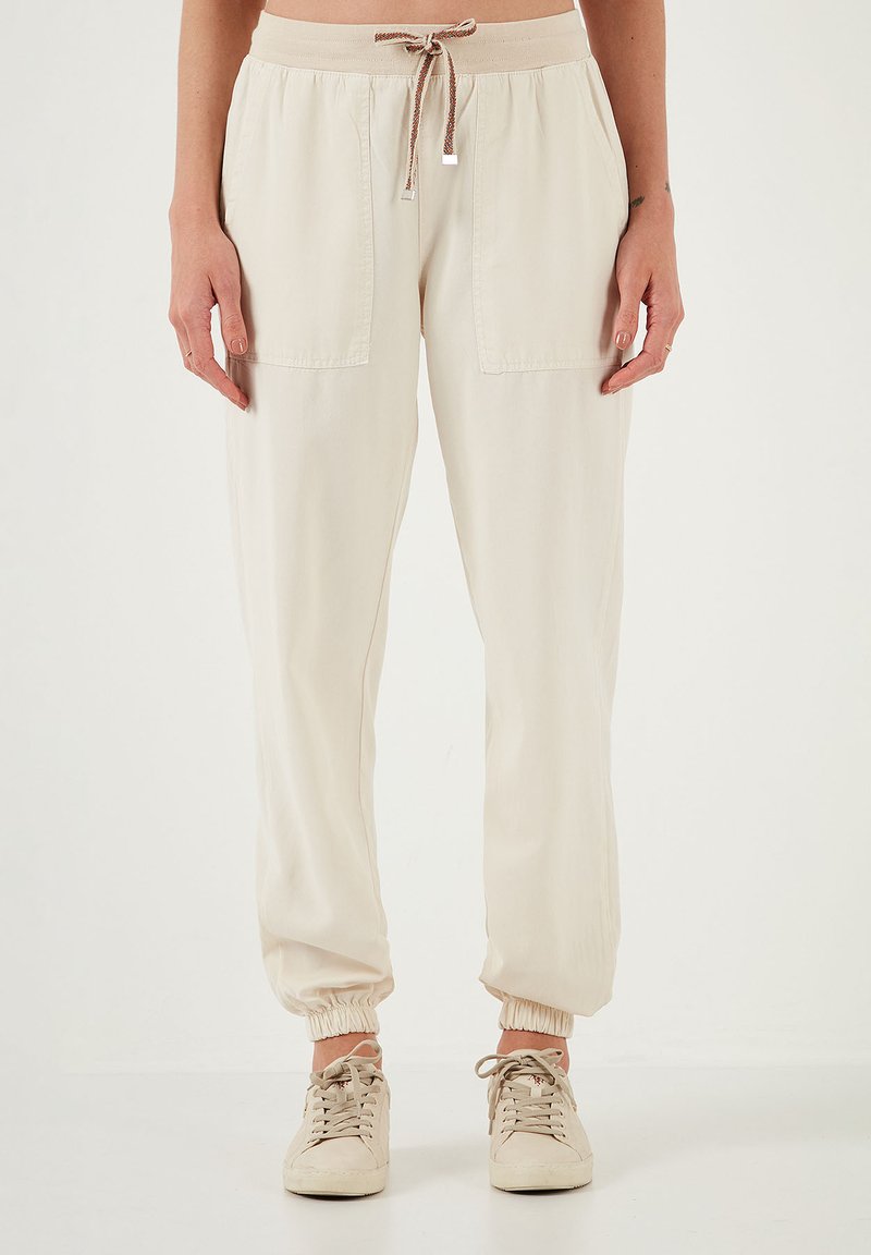 Licht beige joggingbroek met elastische tailleband en drawstring, voorzien van twee grote vo pockets en elastische boorden bij de enkels.