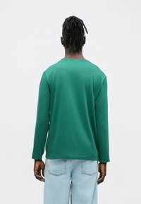 Groen shirt met lange mouwen en een ronde hals, gemaakt van zachte stof. Gecombineerd met lichtblauwe spijkerbroek van denim, met een ontspannen pasvorm en een casual stijl.