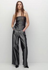 Czarny, odkryty na ramiona top o dopasowanym kroju połączony z luźnymi, szerokimi spodniami o metalicznym wykończeniu; oba mają gładką fakturę i proste szwy.