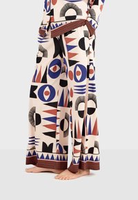 Wide-leg pants with a cream background featuring geometric patterns in red, blue, and black. Includes a striped hem and tie waist detail.