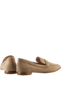 Mocassins en suede beige avec une silhouette incurvée, présentant un rabat sur le cou-de-pied et un petit talon en bois. Texture lisse et détails cousus.