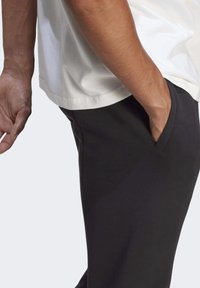 Svarta träningsbyxor i smidig tyg med en sidoficka och en avslappnad passform, tillsammans med en vit t-shirt i bomull.