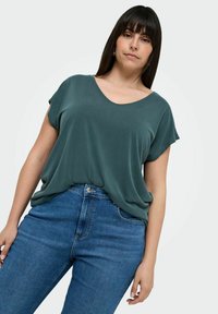 Green, short-sleeve top with a V-neck design made of soft fabric, paired with fitted blue jeans featuring a front button closure and five pockets.