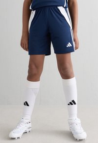 Jūras spēku futbola šorti ar baltām sānu svītrām, ar elastīgu jostu. Baltas zeķes ar melniem akcentiem un baltas sporta kurpes ar zila akcentiem.