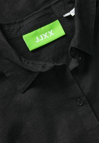 Crna lanena košulja s kragnom, s zelenom oznakom označenom "JJXX" i jednim crnim dugmetom blizu vrata.