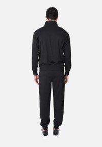 Completo sportivo nero composto da una maglietta a maniche lunghe con colletto e pantaloni coordinati. Realizzato in tessuto morbido con polsini e vita elasticizzati.