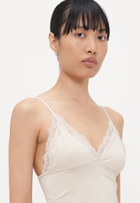 Licht beige bralette met kantafwerking langs de halslijn en banden. Gemaakt van zachte, rekbare stof; heeft een eenvoudig, delicaat ontwerp.