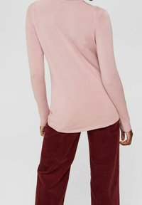 Sweter z długim rękawem w miękkim różowym kolorze o dopasowanym kroju. Połączony z szerokimi, bordowymi spodniami sztruksowymi. Gładka faktura i prosty design.