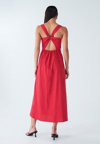 Maxikleid aus leuchtend roter Baumwolle mit Spaghettiträgern und einem geknoteten Rückendetail. Fließende Silhouette mit elastischem Taillenbund und knöchellangem Saum.