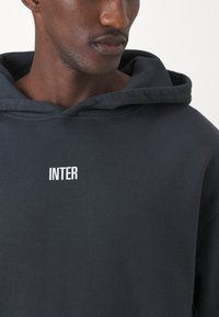 Hoodie cinza escuro feito de algodão, com um grande bolso frontal, capuz com cordão e o logótipo "INTER" em texto branco no peito.