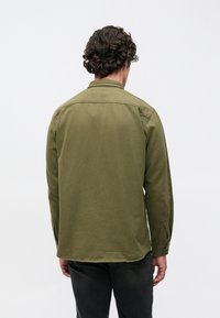 Olívazöld, gombos ing hegyes gallérral, hosszú ujjakkal, hátsó vállrészsel és egymásra gombolt mandzsettákkal. Puha anyag és egyszerű kialakítás.