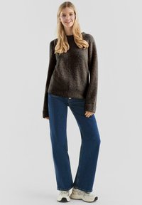 Ciemnoszary, fakturowany sweter z okrągłym dekoltem, zestawiony z szerokimi niebieskimi dżinsami i białymi trampkami. Modelka ma długie włosy i okulary.