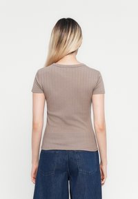 Jeune femme aux longs cheveux ombrés portant un top côtelé taupe à manches courtes ajusté et un jean en denim bleu taille haute, vue de dos.