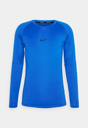 Långärmad blå träningsskjorta i lätt, elastisk tyg. Har en svart Nike-logotyp på bröstet och raglanärmar.