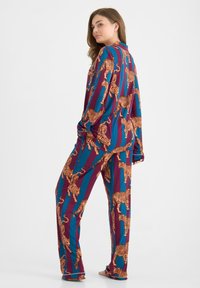 Ensemble de pyjama à manches longues dans un motif vibrant bleu et marron avec des tigres orange. Le tissu semble doux et confortable.