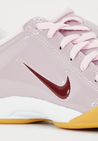Pink patent leather sneaker with a white sole and gum rubber accent, featuring a maroon Nike swoosh and light pink laces.