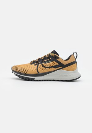 Chaussure de trail Nike beige et noire avec mesh respirant, swoosh noir et semelle blanche amortie, conçue pour la course en extérieur.