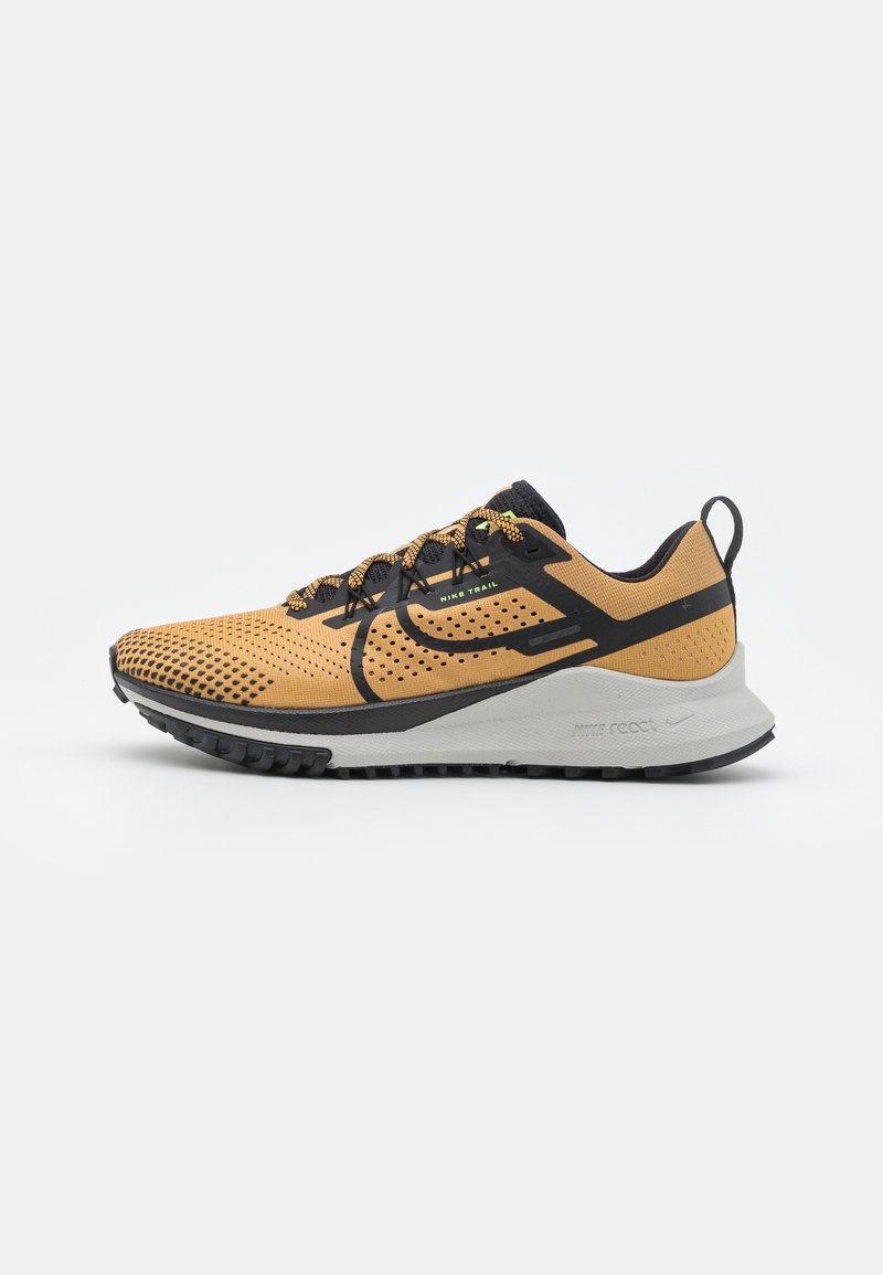 Chaussure de trail Nike beige et noire avec mesh respirant, swoosh noir et semelle blanche amortie, conçue pour la course en extérieur.