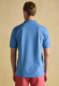 Heledadest t-särk heledas sinises värvitoonis, lühikeste varrukatega, kraega ja seljaosas õmmeldud ümmarguse detailiga. Kombineeritud roosa lühikeste pükstega.